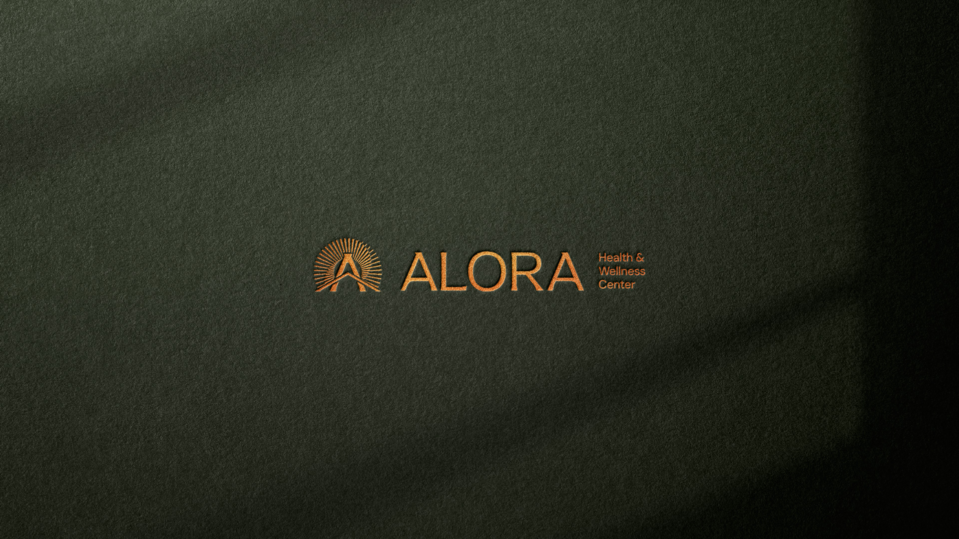 Alora sunburst logo in copper foil on dark olive textured paper