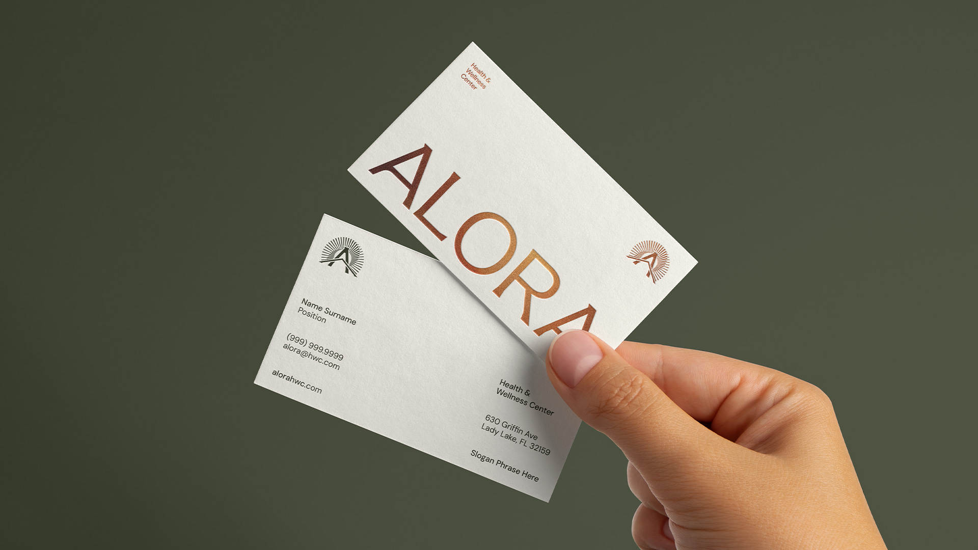 Hand holding two Alora business cards with the wordmark in copper foil