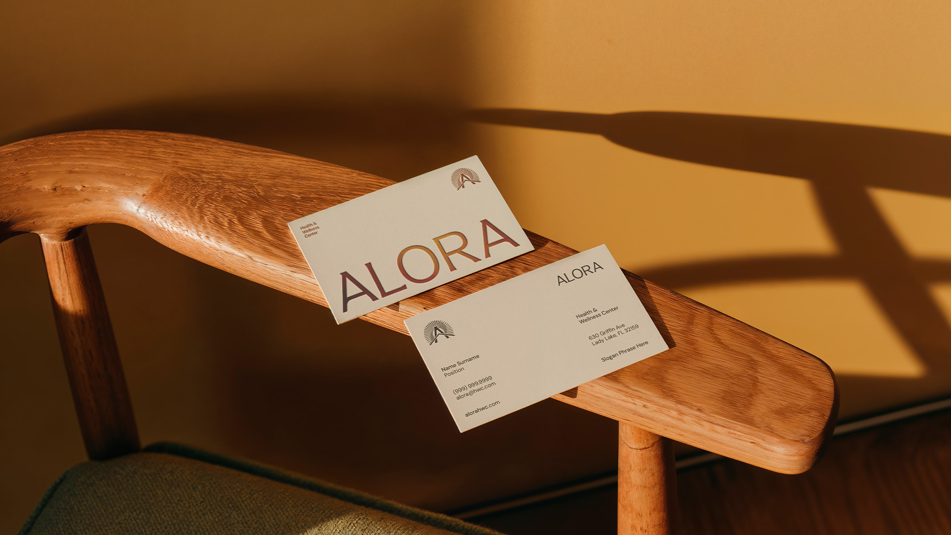 Two Alora business cards resting on a wooden chair arm in warm afternoon light