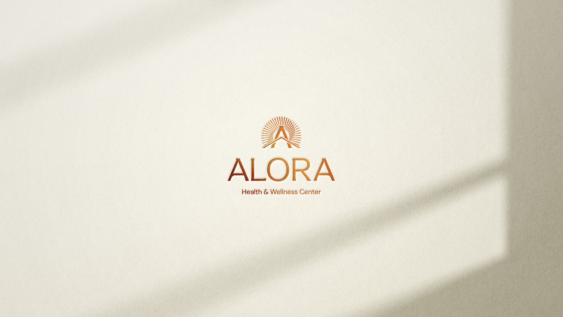 Alora Health & Wellness Center logo in copper foil on cream textured paper, lit by window light