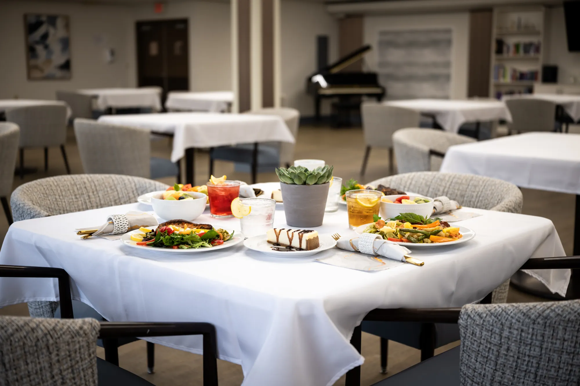 The Amara dining room set with white linen, plated meals and a piano in the background