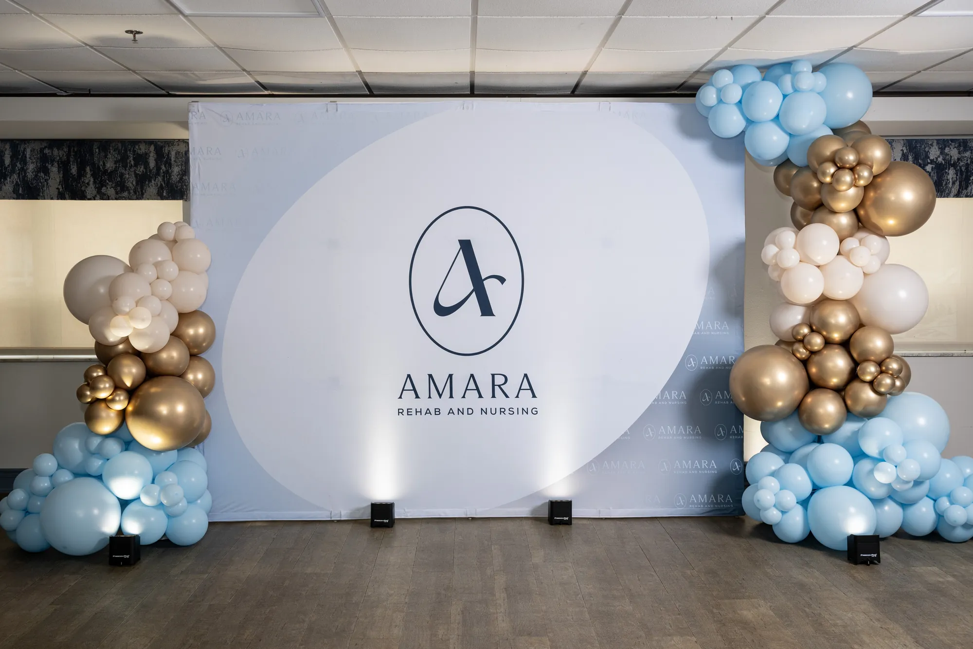 The Amara step and repeat backdrop framed by a blue and gold balloon garland