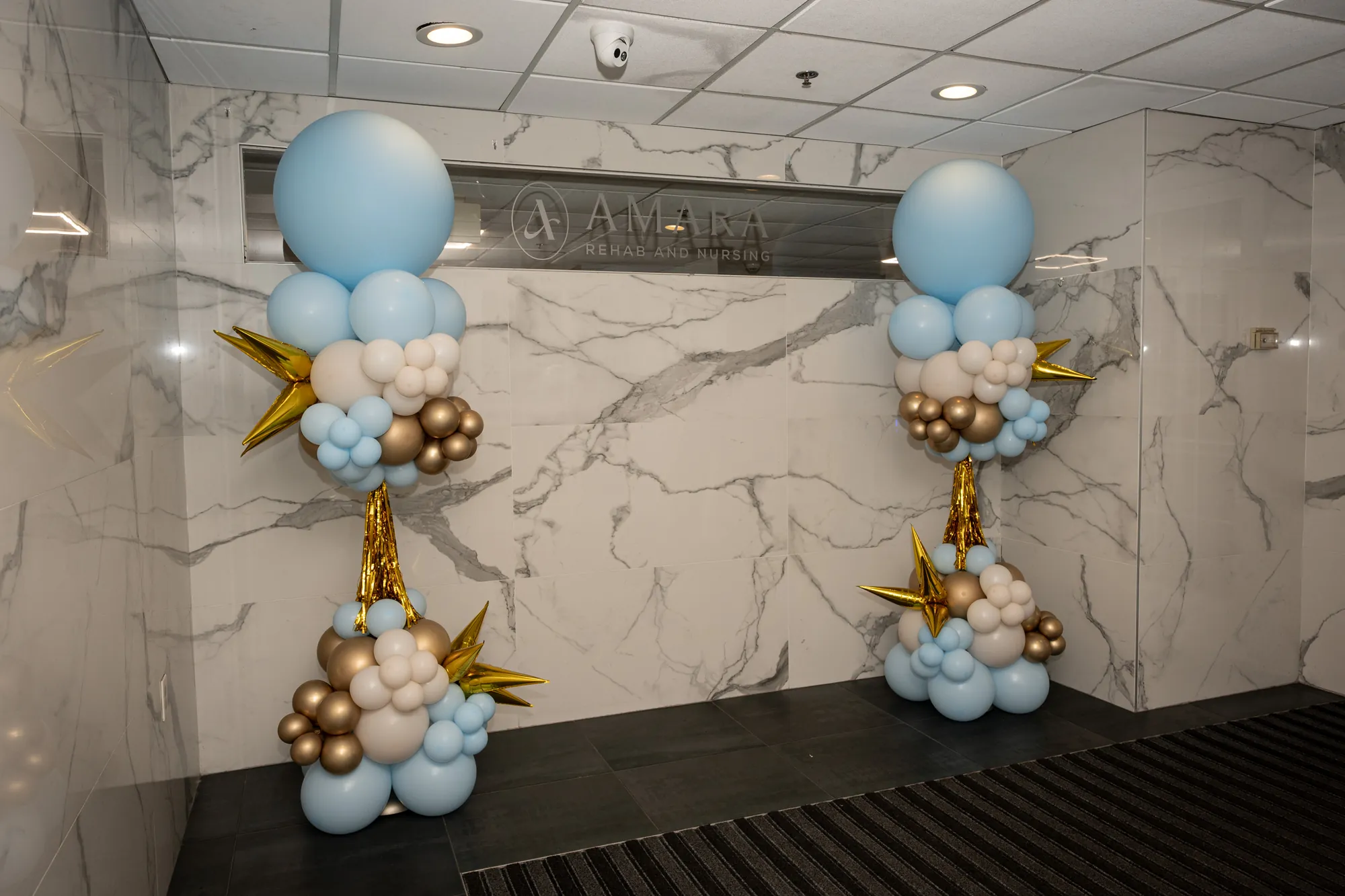 Blue and gold balloon columns flanking the marble entry wall at the Amara open house
