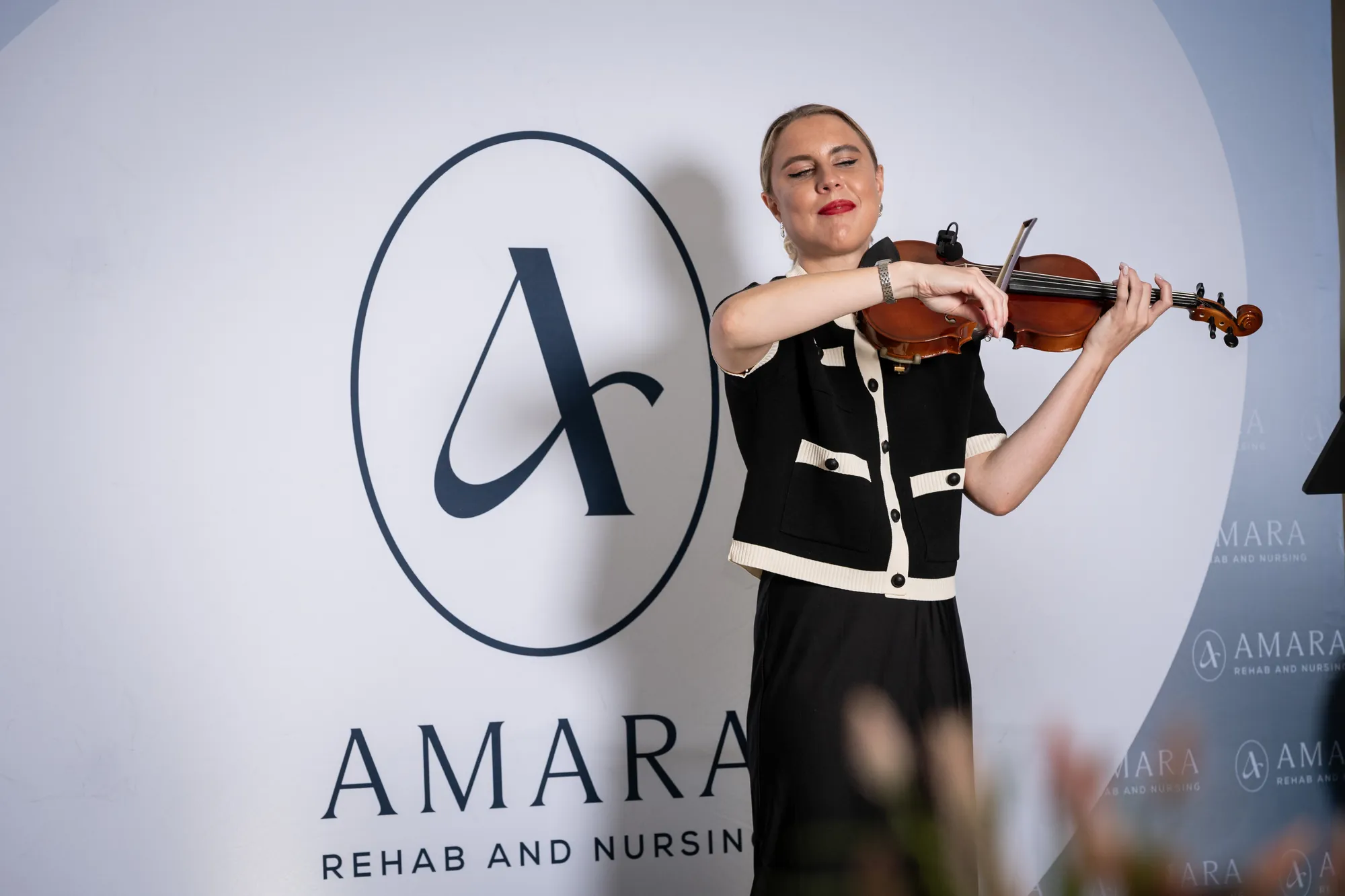 A violinist playing in front of the Amara Rehab and Nursing step and repeat
