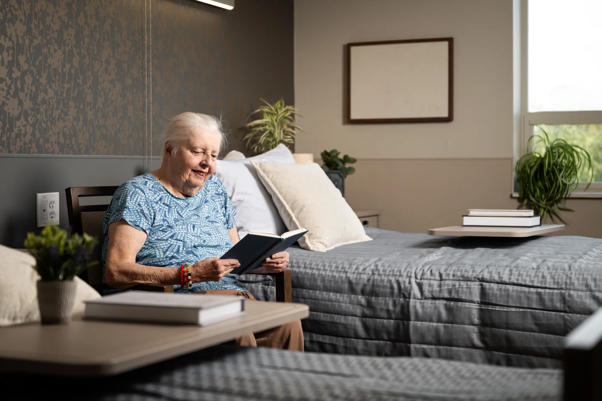 A resident sitting on her bed at Amara reading a book in afternoon light