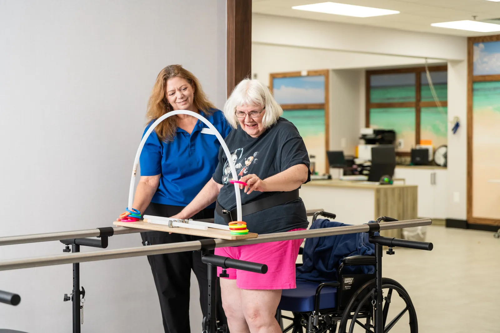 Therapist supporting a resident through a ring-stacking exercise on parallel bars