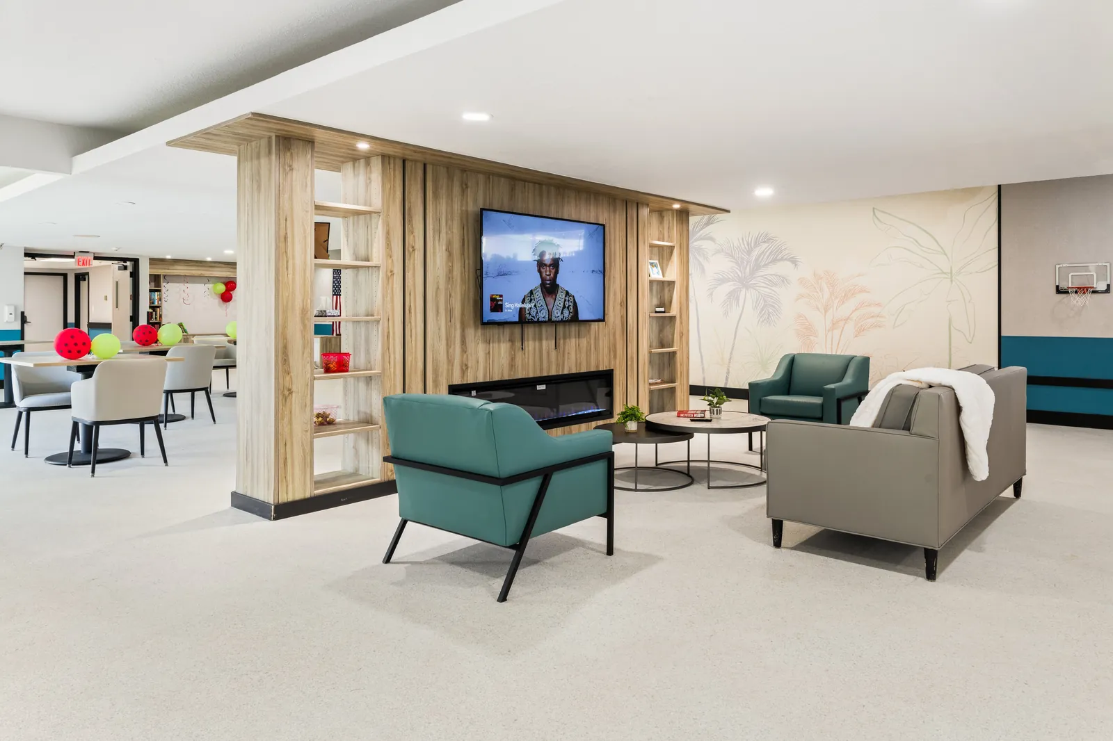Carlton Shores tv and fireplace lounge with green chairs and palm wall mural