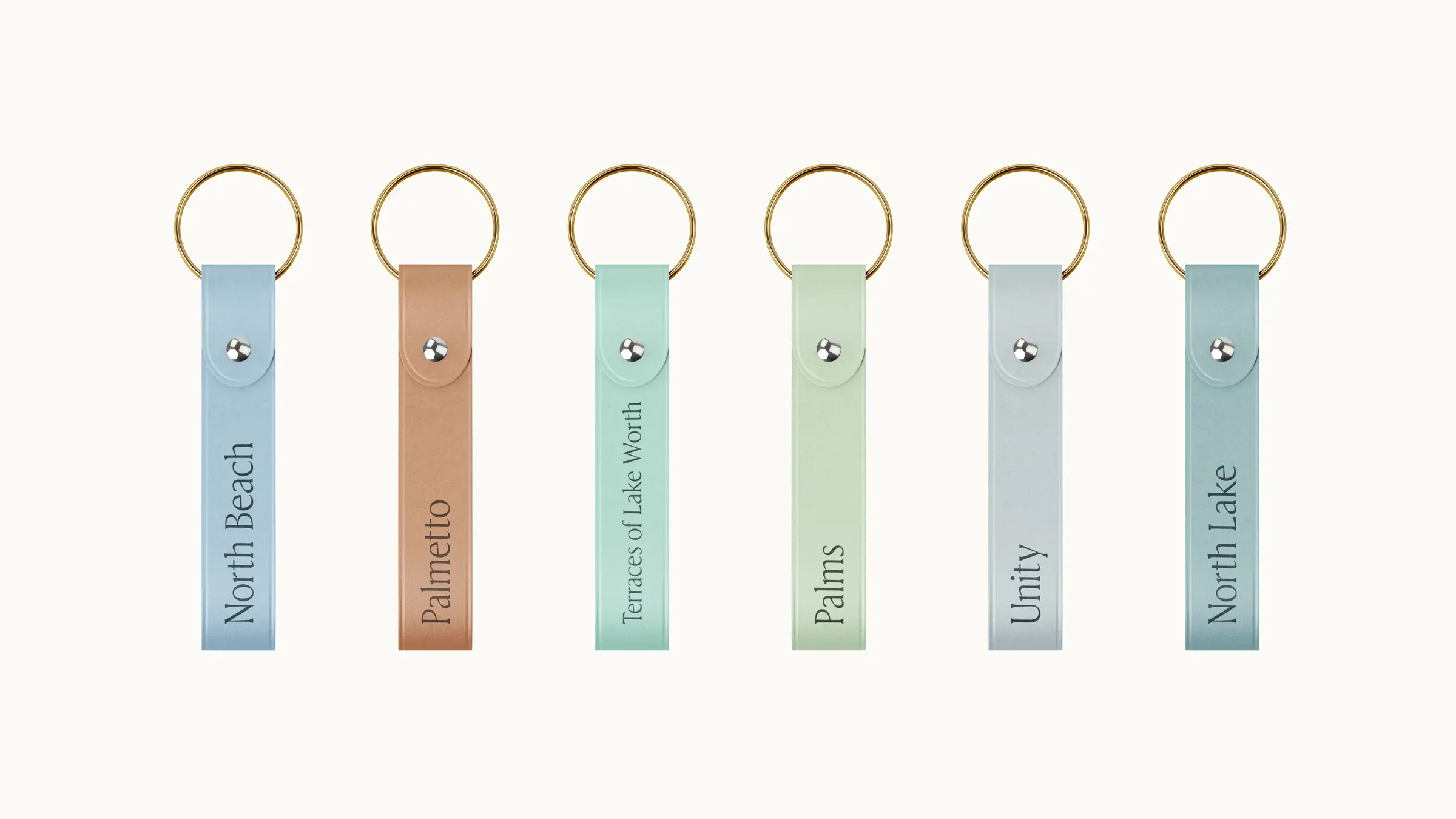 Six branded keychains in soft pastel leathers, each engraved with a facility name in serif type