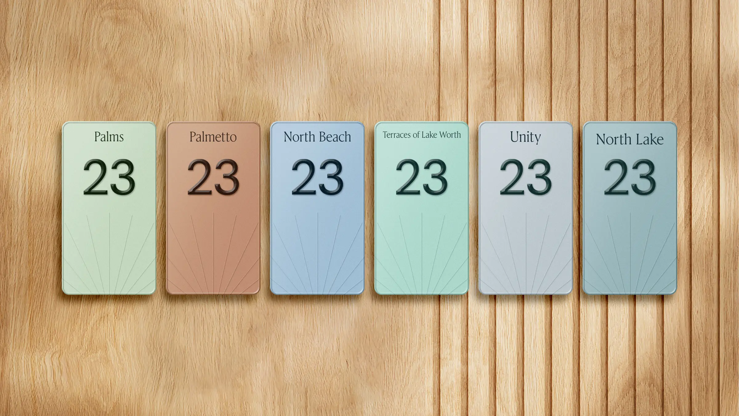 Six pastel room number plaques mounted on warm wood paneling, each numbered 23 in serif type with the facility name above