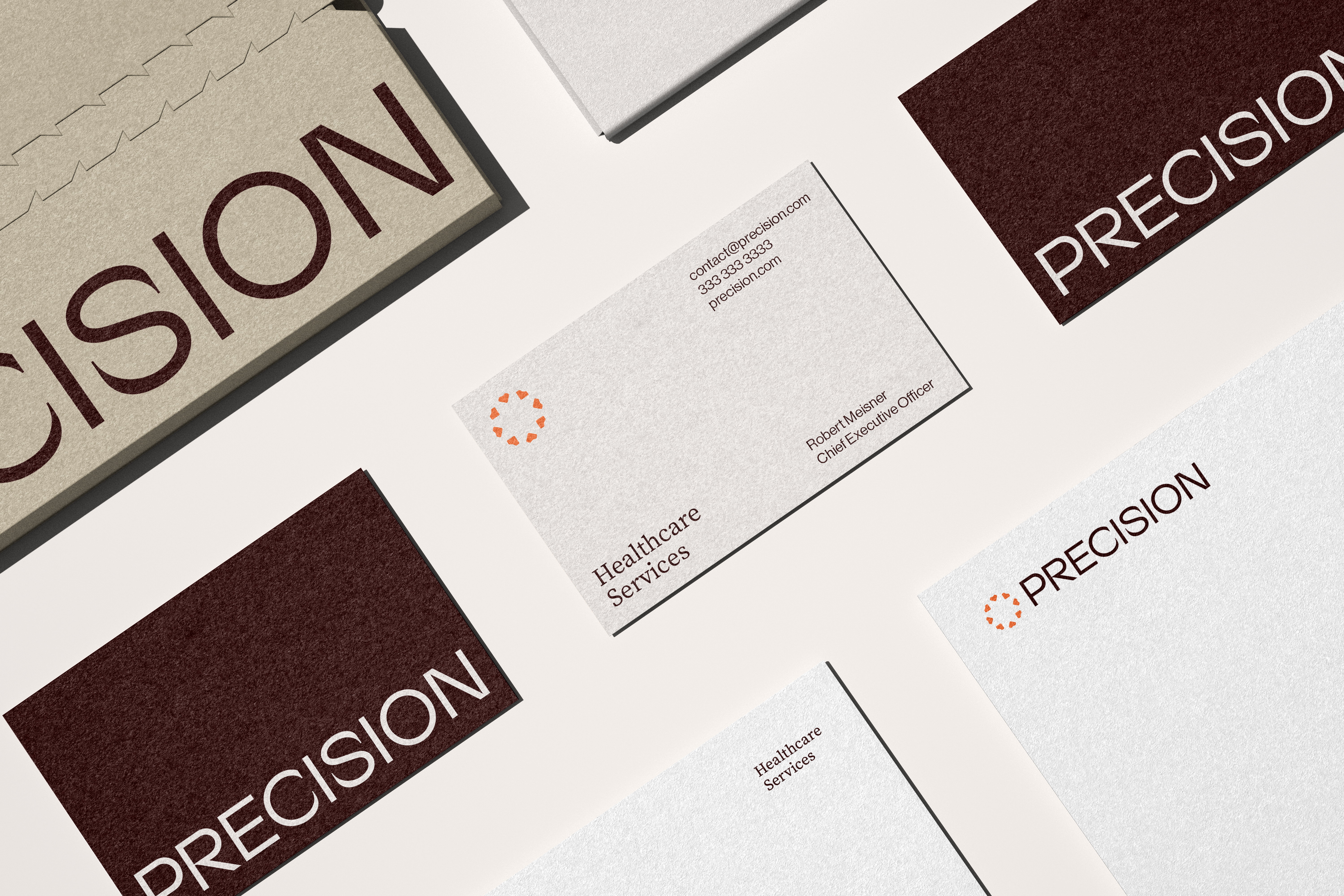 Angled flat lay of Precision cards, folder, and letterhead in oxblood, kraft, and grey
