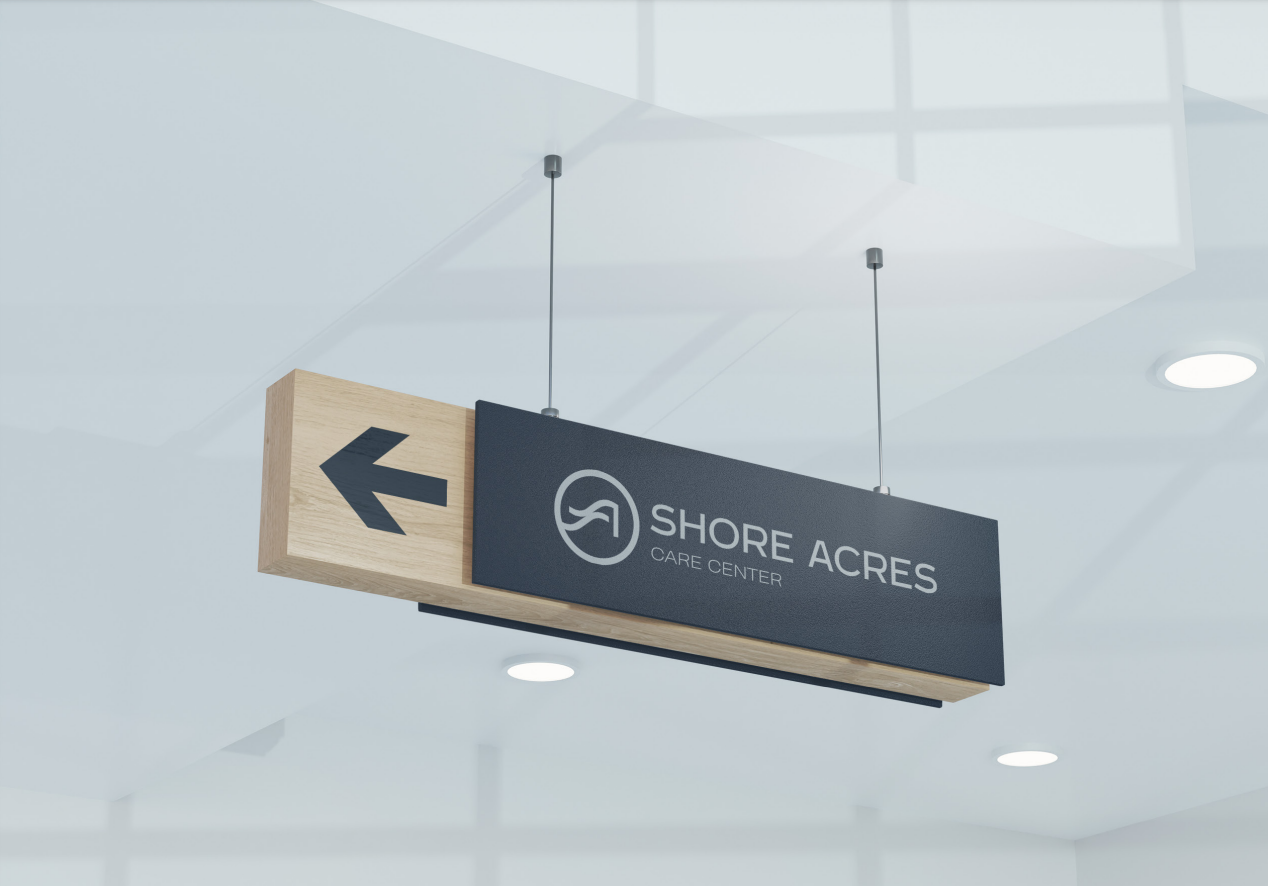 Suspended Shore Acres Care Center wayfinding sign in navy and oak, with a directional arrow