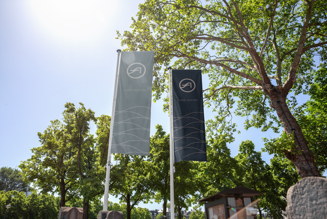 Two Shore Acres Care Center flagpole banners in grey and navy against summer trees
