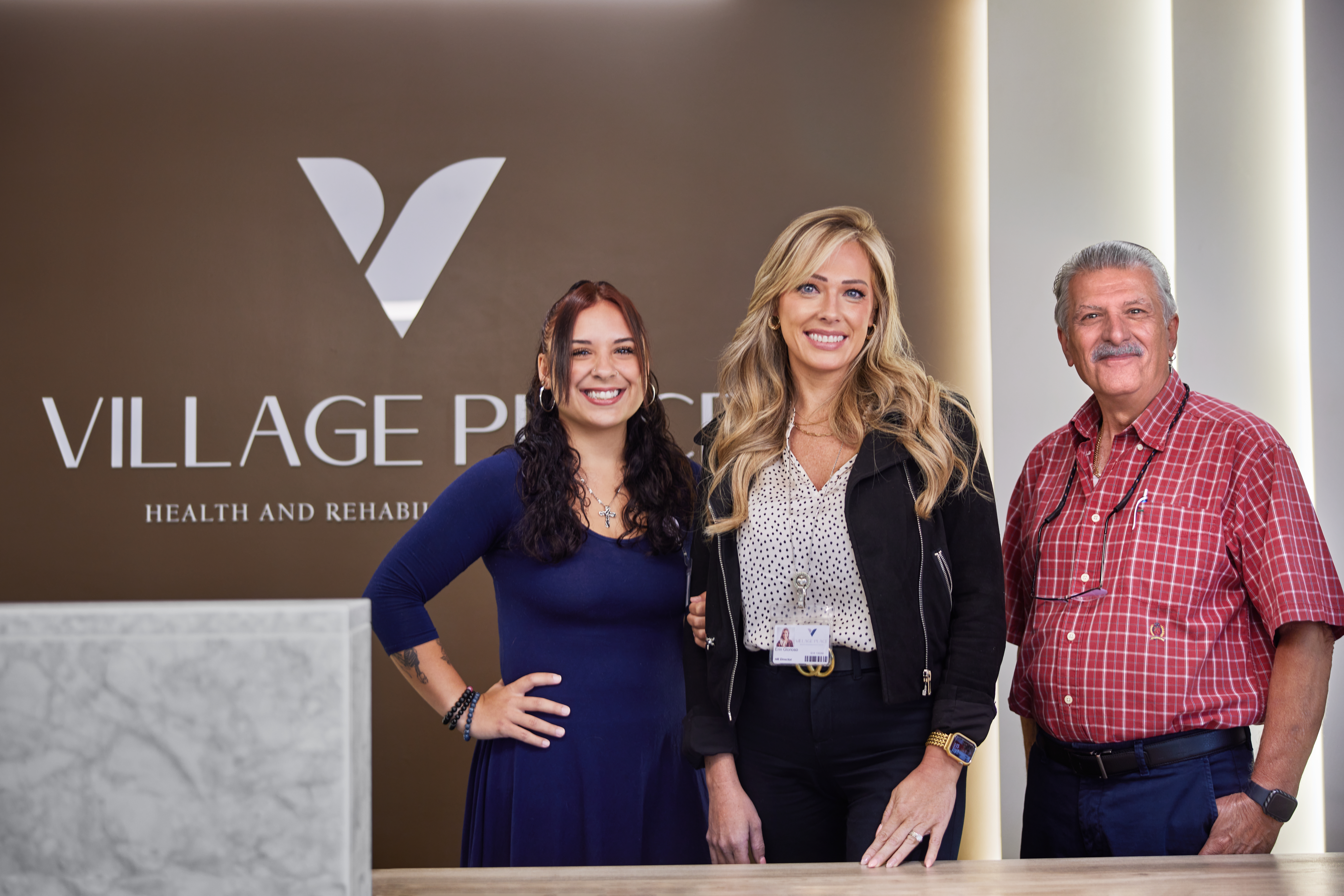 Three Village Place team members at the reception desk under the brand mark
