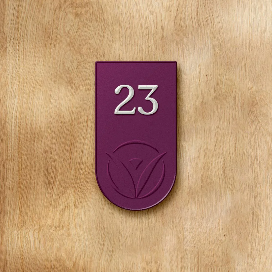 A purple Vivo Healthcare door tag on a wood door, room 23, with the mark cut into the base